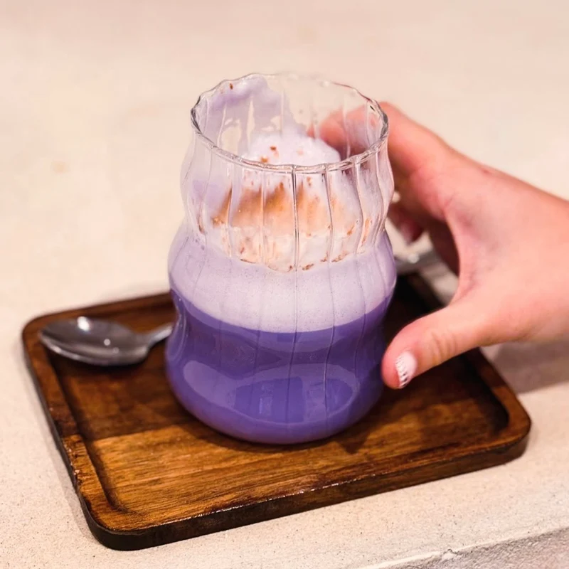 Ube Nolia ube latte in a ribbed glass on a wooden tray